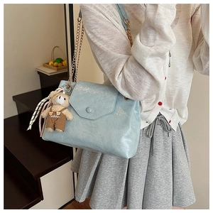 Détail du sac à main bleu clair en cuir craquelé avec chaîne dorée et breloque ours