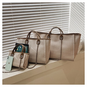 Set de tres bolsos tipo cubo de lona beige con ribete de cuero marrón y cadena plateada