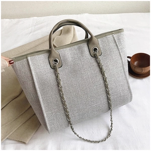 Detalle del bolso tote de tweed gris con ribete de cuero y correa de cadena plateada
