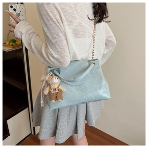 Sac à bandoulière plissé bleu clair avec chaîne dorée et breloque ours sur modèle