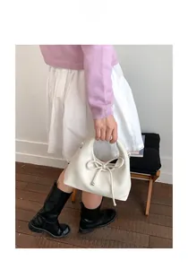 Detailed shot of white leather handbag featuring minimalist bow decoration and top handle