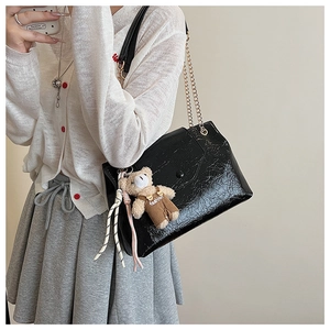 Détail du sac à bandoulière plissé noir brillant avec chaîne dorée et breloque ours