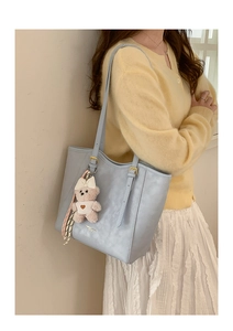 Detail of light blue tote bag with plush bear charm and embossed logo on PU leather