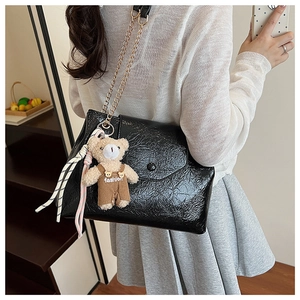 Sac bandoulière noir plissé avec chaîne dorée et breloque ours porté par un mannequin