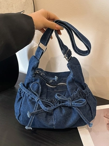 Blue denim crossbody bucket bag with bow accents and adjustable strap in a casual setting