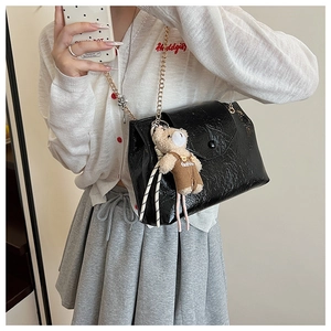 Détail du sac cabas en cuir verni noir avec chaîne dorée et charmant pendentif ours en peluche