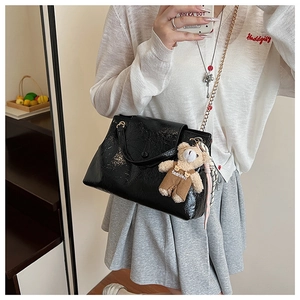 Détail d'un sac à main noir brillant avec chaîne dorée et charmant ourson en peluche