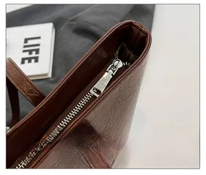 Detail eines silbernen Reißverschlusses und Logos auf einer braunen Leder-Tragetasche
