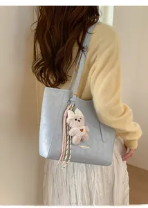 Detail of light blue leather tote bag with plush bear charm and ribbon on shoulder strap