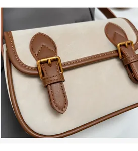 Gros plan des coutures contrastées et de la boucle dorée sur un sac bandoulière crème