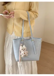 Close-up of light blue tote bag with plush bear charm and fashion leather logo detail