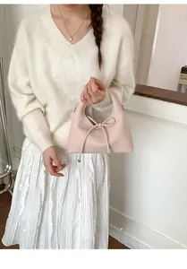 Detail of soft pink leather handbag with decorative bow knot and curved top handle