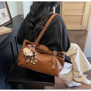 Gros plan d'un sac cabas en cuir marron grainé avec charm ours et bandoulière réglable