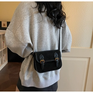 Détail du sac bandoulière noir en aspect daim avec doubles boucles dorées et rabat
