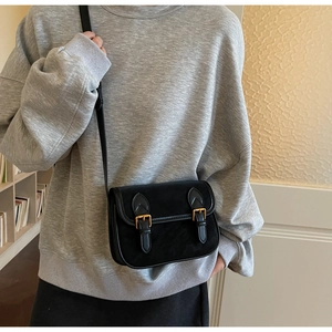 Gros plan d'un sac bandoulière en daim noir avec boucles dorées porté par un mannequin
