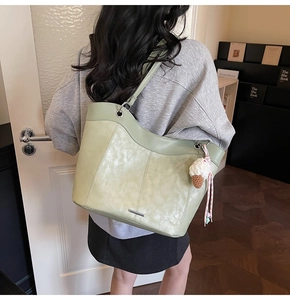 Detail of light green suede tote bag with metal bar and ice cream charm on shoulder