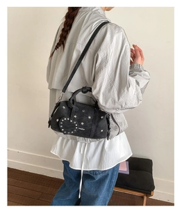 Detail of black leather pillow bag featuring star rivets and a heart charm with shoulder strap