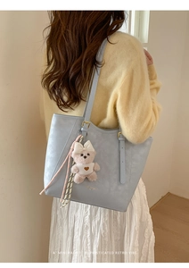 Detail of light blue faux leather tote bag with a pink plush bear charm and heart print