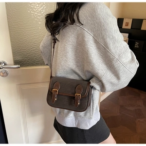 Détail du sac bandoulière vintage avec bordures contrastées et boucle en métal sur modèle
