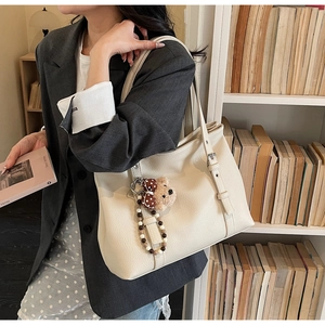 Détail d'un grand cabas crème en cuir grainé avec breloque ours et sangle à boucle métal