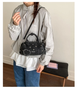 Detail of black Boston bag with star rivets and heart charm worn by a model