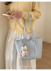 Detail of light blue faux leather tote bag featuring a plush bear charm and long strap