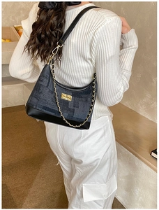 Detail view of retro denim hobo bag with gold chain strap worn by a female model