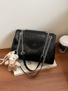 Sac à bandoulière noir plissé brillant avec breloque ours mignon sur table en bois