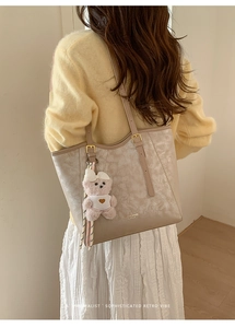 Detail of beige tote bag with subtle floral texture and cute pink plush bear charm