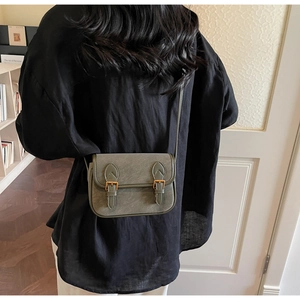 Détail du sac à bandoulière en cuir vert olive avec deux boucles métalliques sur modèle