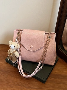 Sac sous le bras plissé rose avec chaîne dorée et breloque ours sur des livres