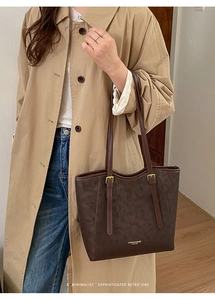 Detail of dark brown tote bag showing smooth leather texture and metallic strap buckle