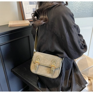 Détail d'un sac messager vert sauge avec boucles dorées et texture grainée