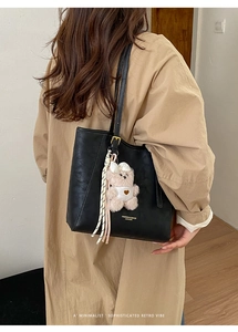 Detail of black faux leather tote bag with plush bear charm and ribbon on model