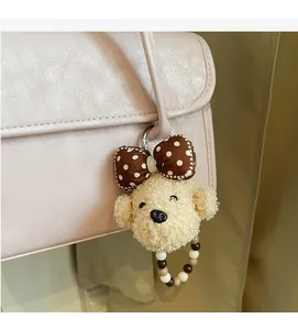 Detail of a beige teddy dog plush pendant with a polka dot bow on a pink leather bag