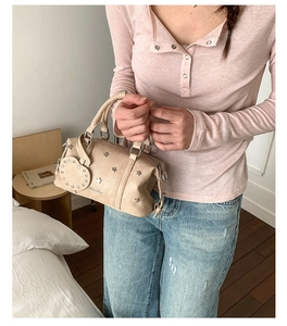 Detail of beige Boston handbag with star studs and heart charm in a lifestyle setting