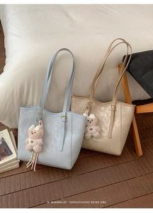 Close-up of minimalist tote bags in blue and beige with bear charms on a chair