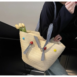 Détail du cabas en paille tressée avec pompons colorés et anses en tissu rayé