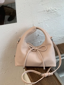 Elegant beige handbag with bow ribbon detail and circular handle on a minimalist background