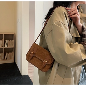 Sac bandoulière rétro marron avec bandoulière réglable porté sur un trench-coat kaki