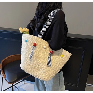 Détail du sac en paille tissée avec pompons colorés et bandoulière rayée de plage