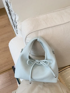 Light blue bow-knot leather handbag with litchi texture on a cozy fabric background