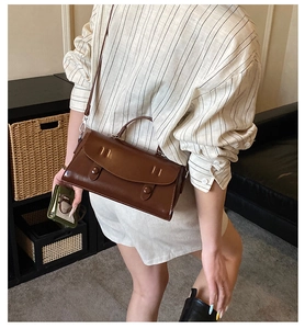 Detail of vintage brown glossy leather baguette bag worn by model in cozy home setting