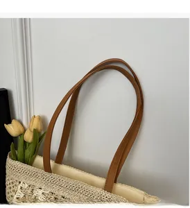 Detail of woven straw tote bag featuring brown faux leather straps and floral patterns