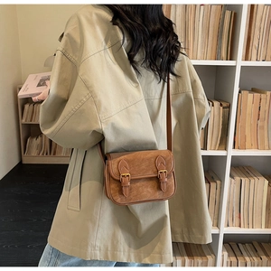 Détail d'un sac bandoulière marron rétro avec boucles dorées porté sur un trench beige