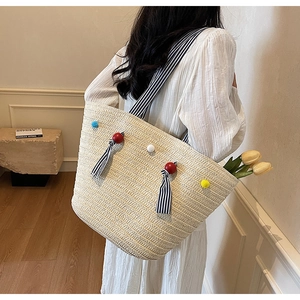 Gros plan du sac cabas en paille avec pompons colorés et rubans rayés détaillés