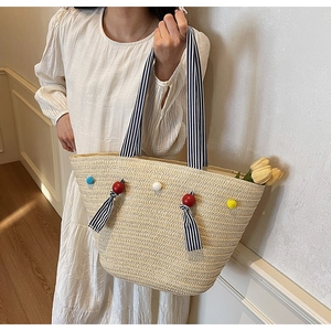 Détail du sac cabas en paille tissé avec pompons colorés et anses ruban rayées