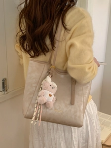 Large beige PU leather tote bag with plush bear charm worn by a model in casual setting