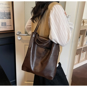 Détail d'un grand cabas en cuir marron foncé porté par un mannequin dans un bureau chaleureux
