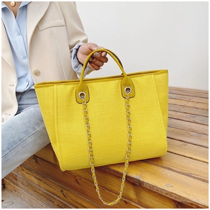 Detalle del bolso tote tejido amarillo con cadena plateada mostrado en un ambiente real